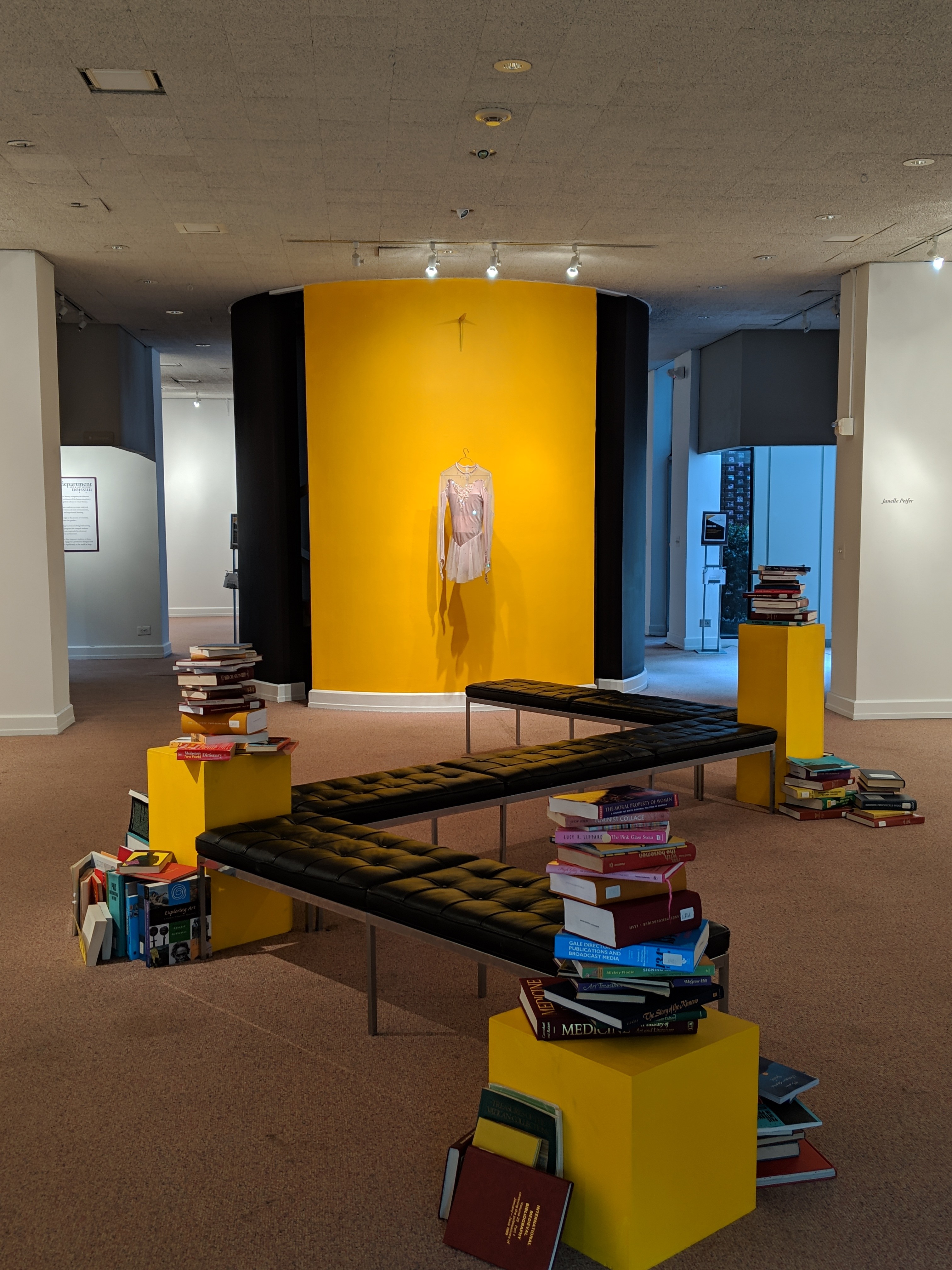 entrance of the gallery. three yellow stands stacked with books and connected to several benches for visitors pleasure.